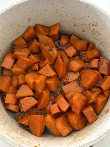 A pot of quartered sweet potatoes in a brown sugar butter glaze.