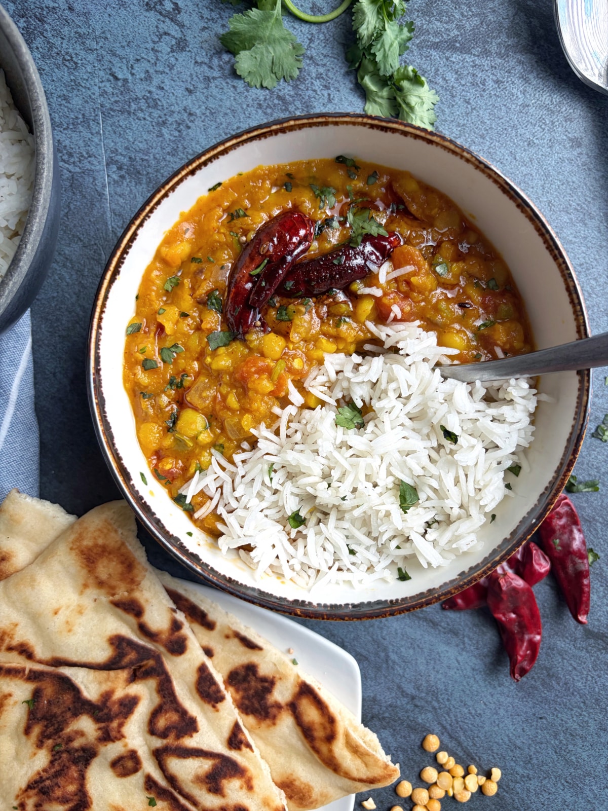Dal Tadka in a bowl with basmati rice, and other accompaniments on serving dishes on the side.