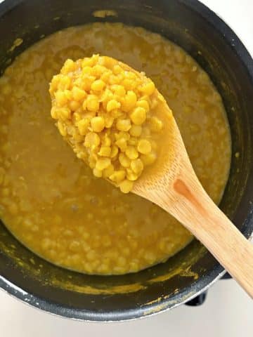 Cooked lentils in a wooden spoon suspended over the rest of the pot.