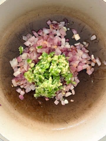 A skillet with sautéed onions and crushed aromatics like peppers and ginger.