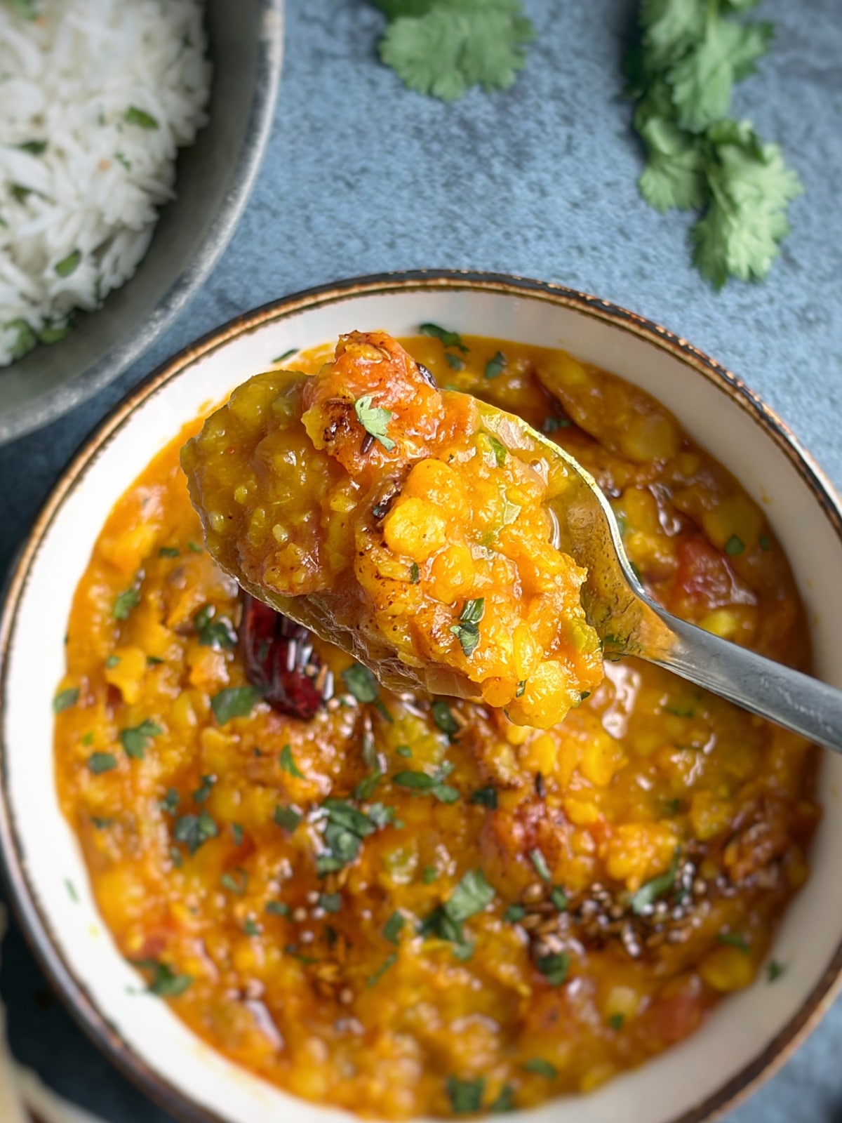 A spoonful of Indian yellow lentil curry held over the rest of the serving bowl.