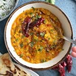 A bowl of Indian lentil curry, known as dal tadka, with dried red chilies and fresh herbs on top.