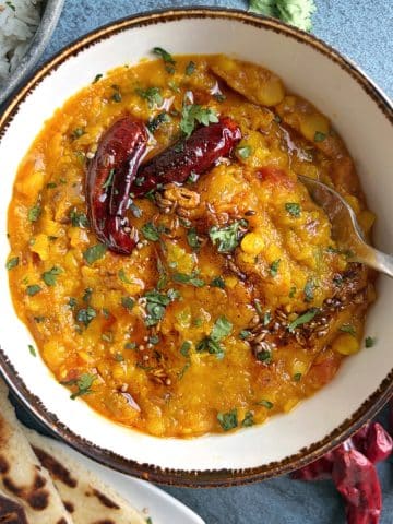 A bowl of Indian lentil curry, known as dal tadka, with dried red chilies and fresh herbs on top.