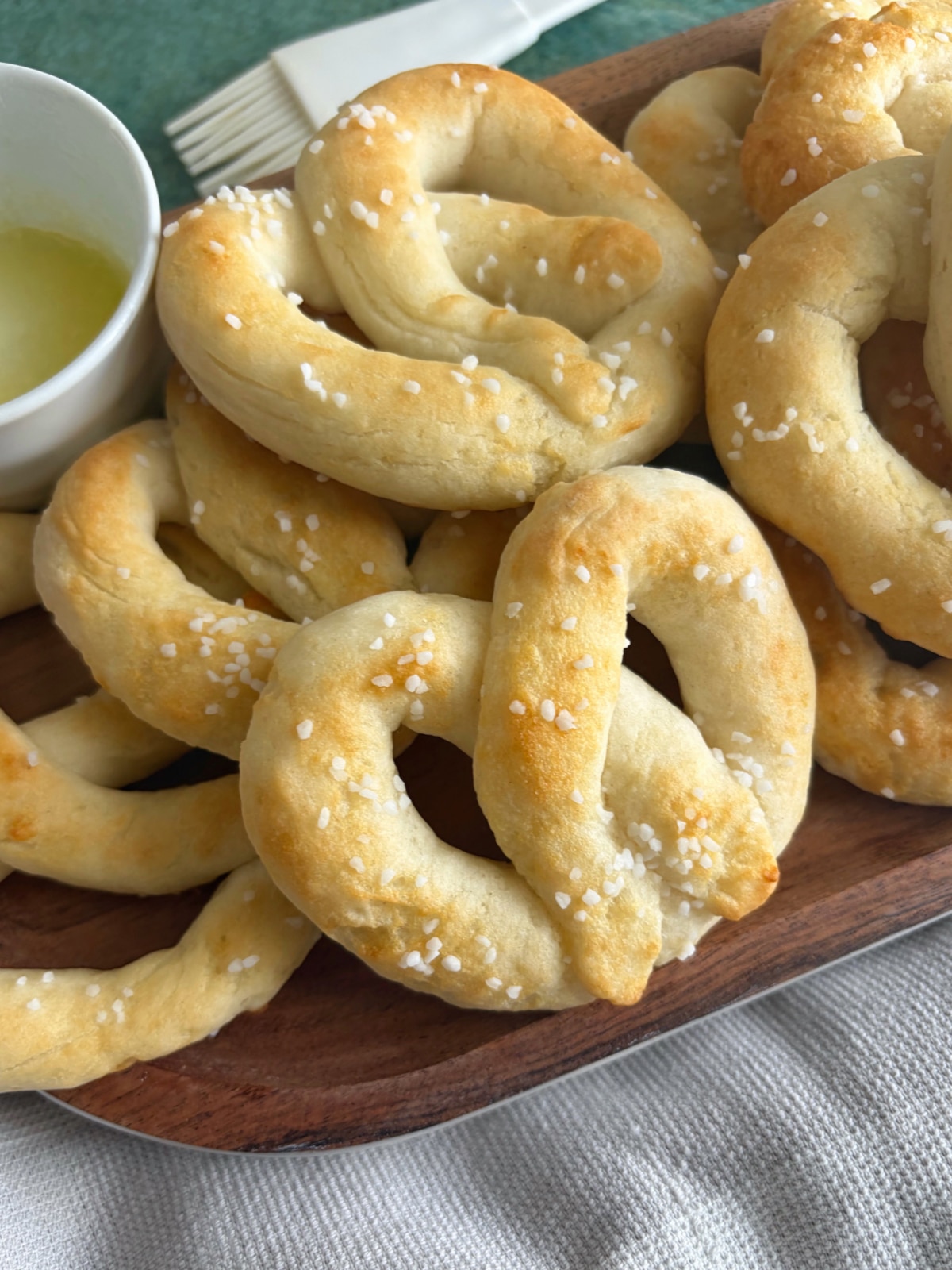 A tray of baked soft pretzels with a side of melted butter.