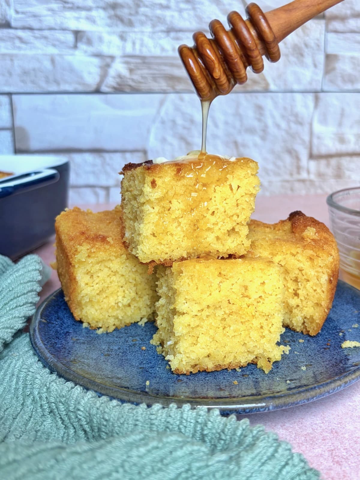 Honey being drizzled on top of a stack of square cornbread pieces on a plate.