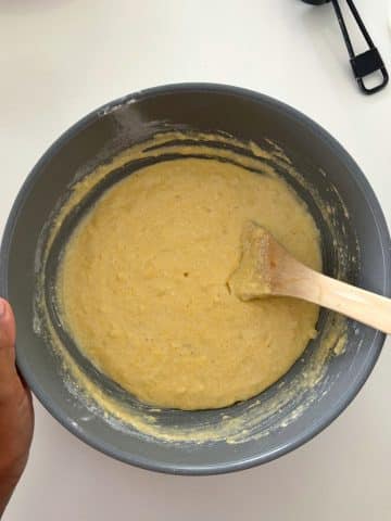 A mixing bowl with cornbread batter and a wooden spoon inside.