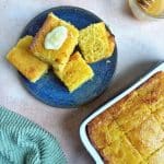 A plate of honey butter cornbread squares with the pan in the bottom right corner.