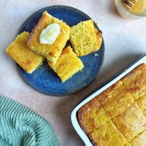 A plate of honey butter cornbread squares with the pan in the bottom right corner.