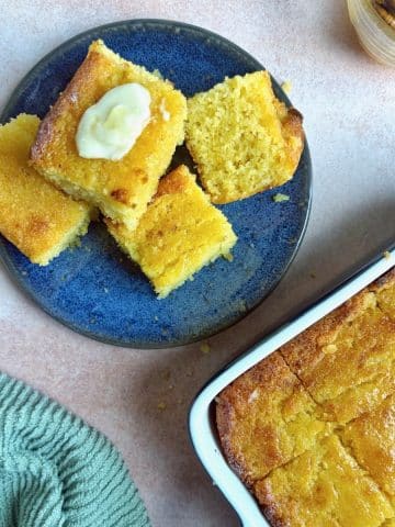 A plate of honey butter cornbread squares with the pan in the bottom right corner.