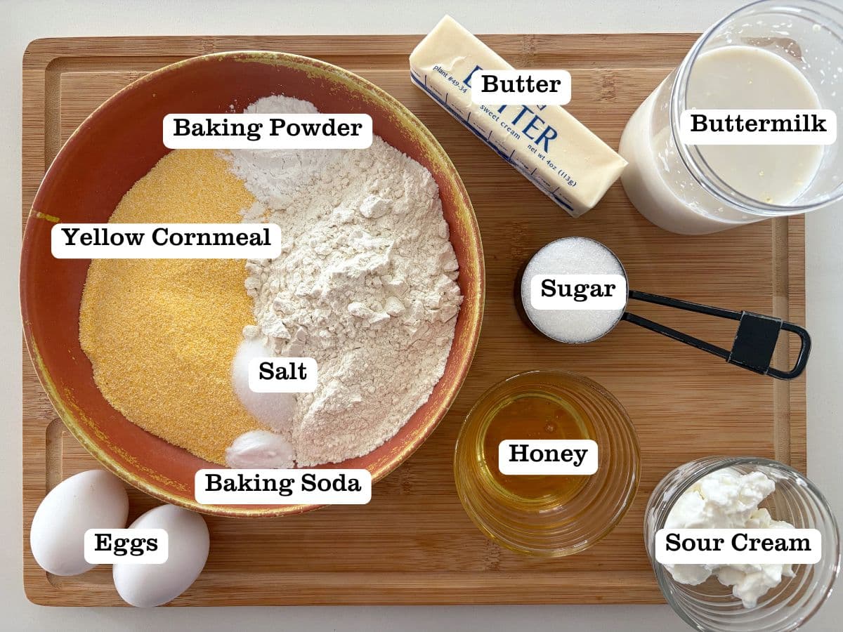 A wooden board with containers of ingredients to make honey butter cornbread.
