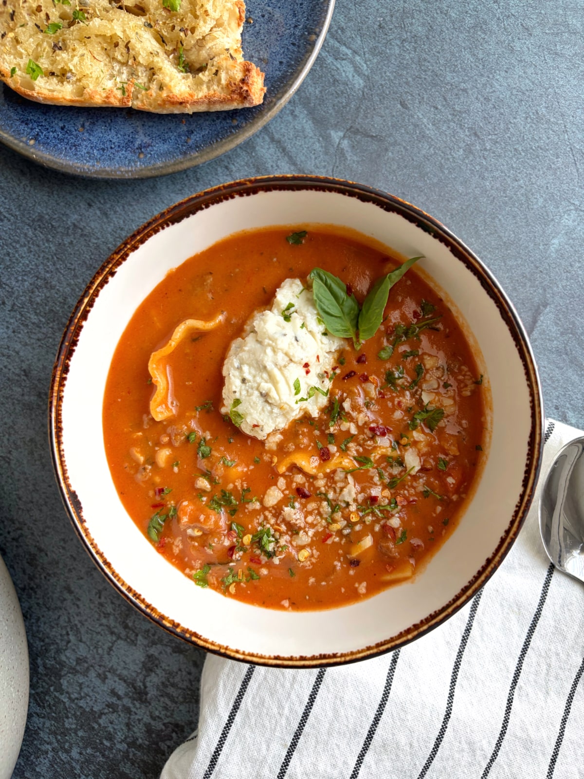 A bowl of lasagna soup with a piece of garlic bread on the side.