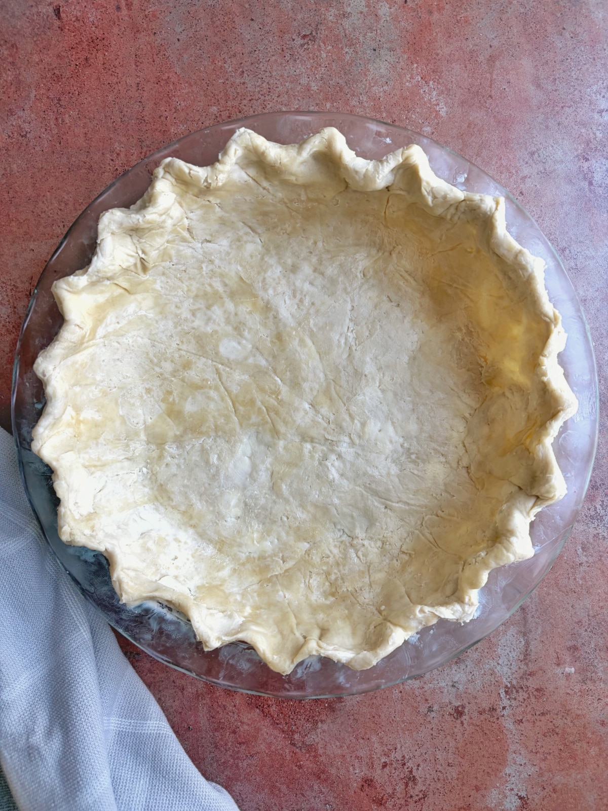 A crimped and fluted pie crust dough in a glass dish, before baking.