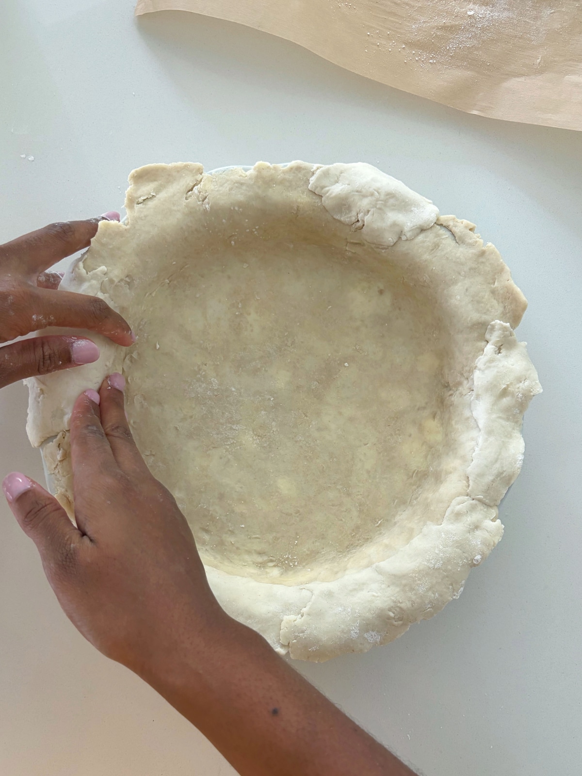 Two hands shaping a homemade pie crust into a pie dish.