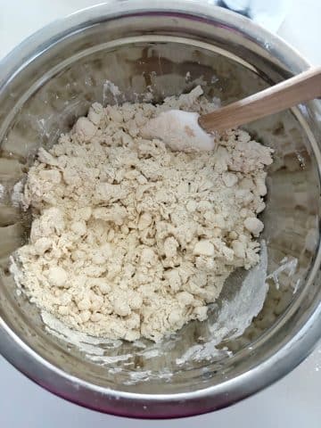 A stainless steel bowl with pieces of butter-coated flour.