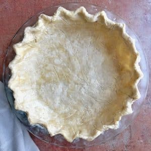 A glass pie dish with homemade butter pie crust shaped inside, before baking.