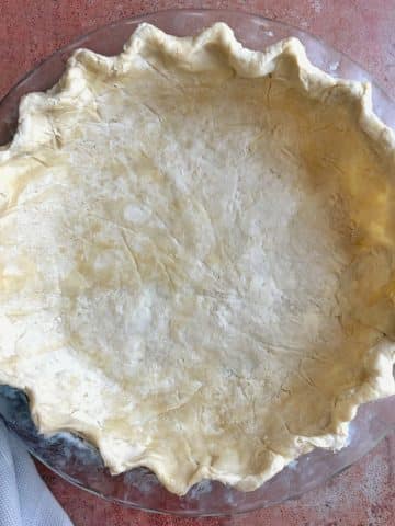 A glass pie dish with homemade butter pie crust shaped inside, before baking.