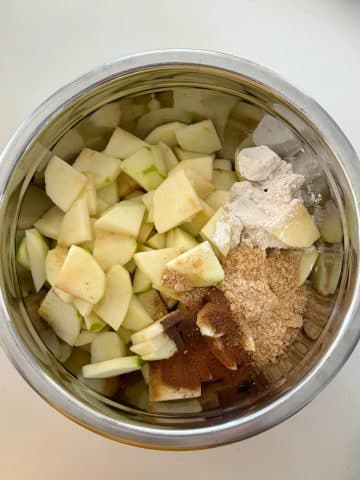 A mixing bowl with sliced apples, spices, lemon juice, and flour.