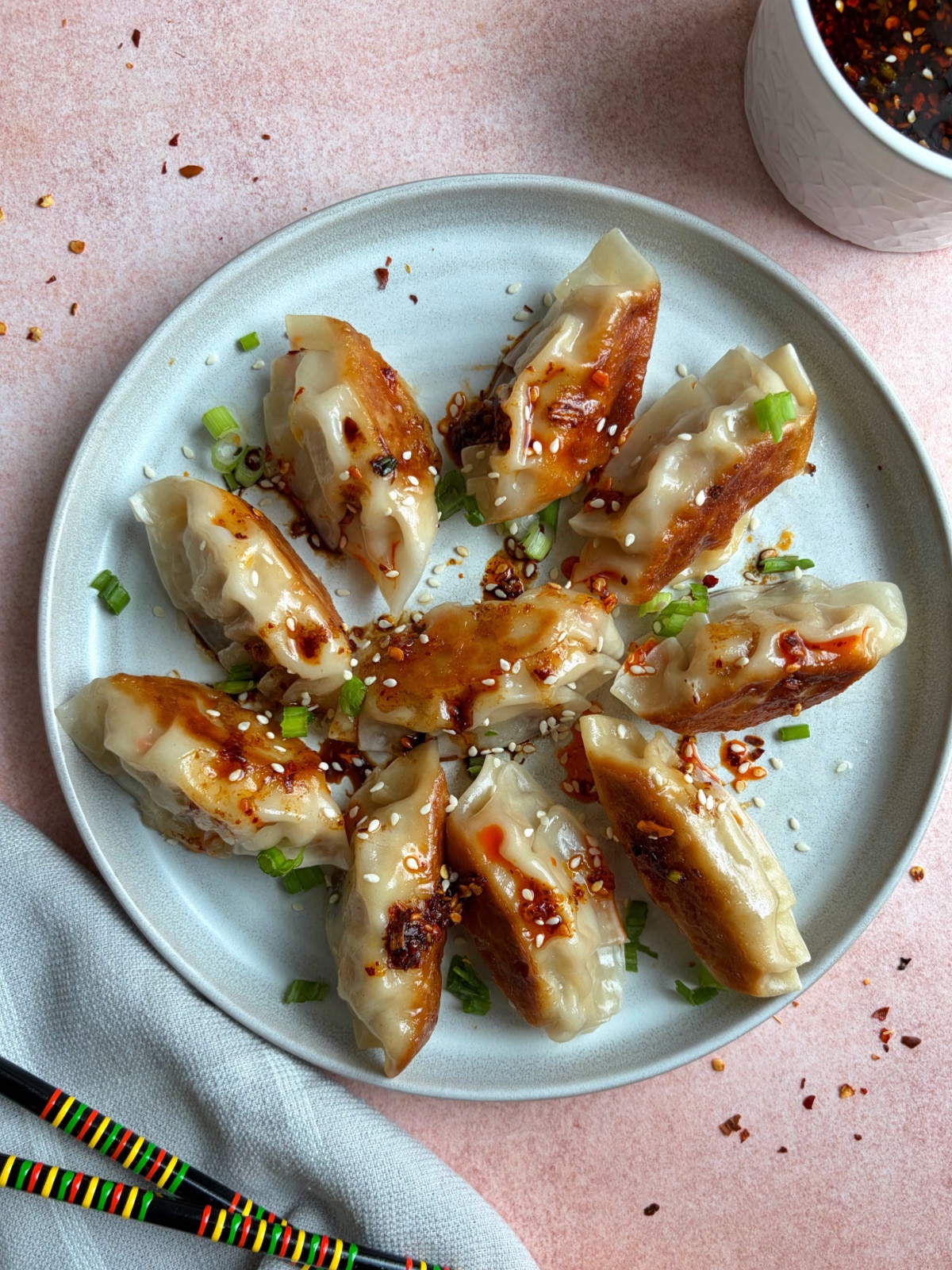 A plate of Asian chicken dumplings with chili oil and green onions.