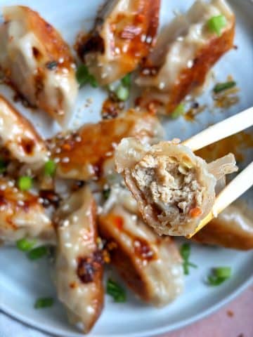 A pair of chopsticks holding up a chicken dumpling with a bite taken out of it to show the interior.
