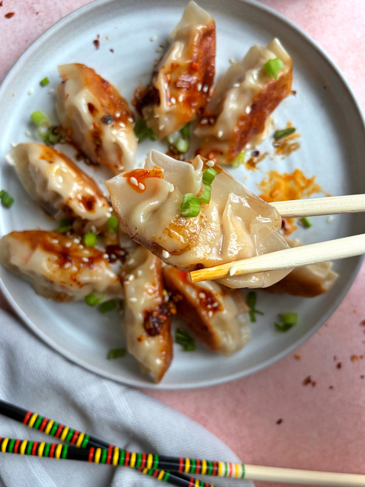 A pair of chopsticks holding up a steamed dumpling over the rest of the plate.