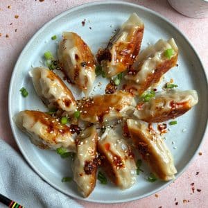 A plate of Asian chicken dumplings arranged in a circle with chili oil and green onions on top.