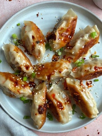 A plate of Asian chicken dumplings arranged in a circle with chili oil and green onions on top.