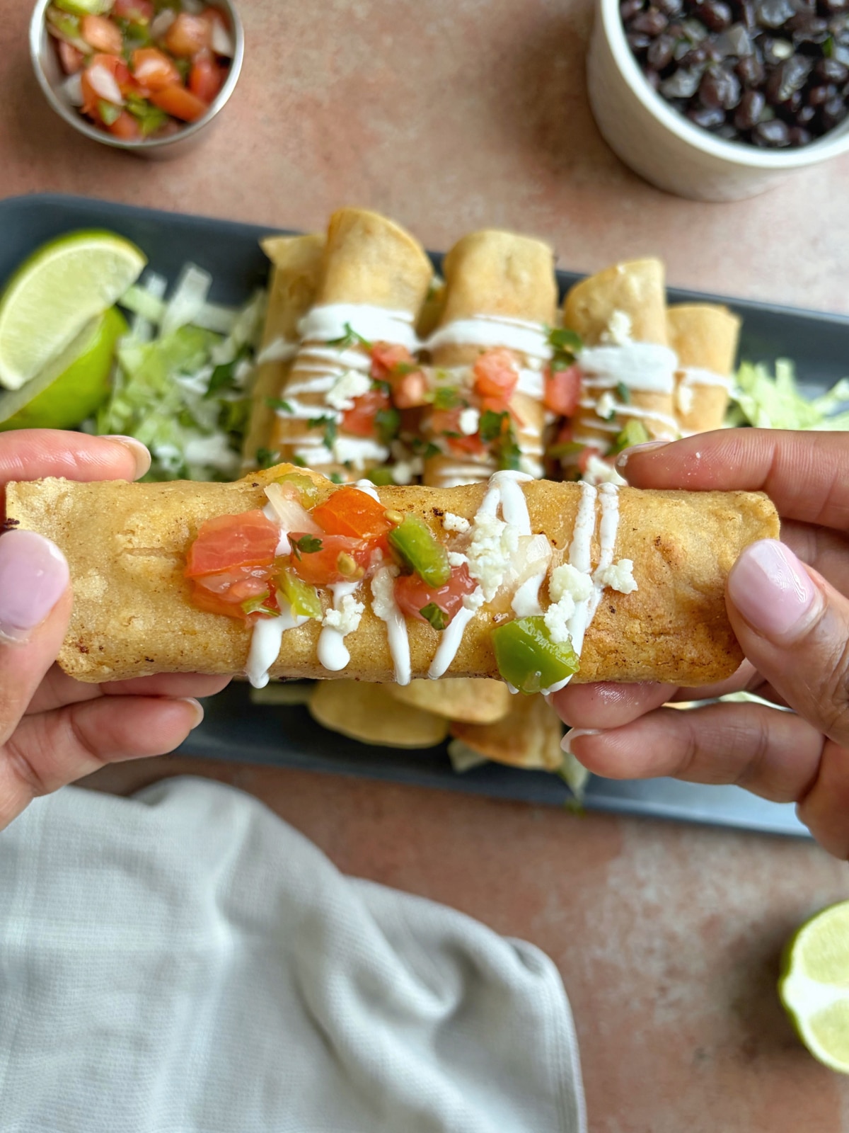 Hands holding a homemade shredded chicken taquito.