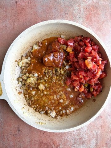 A skillet with diced tomatoes, sautéed veggies, and dried spices.