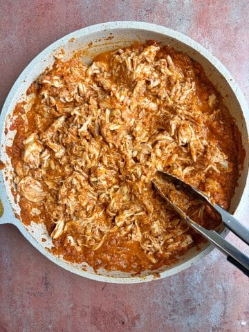 A skillet with shredded chicken tossed in a tomato sauce.