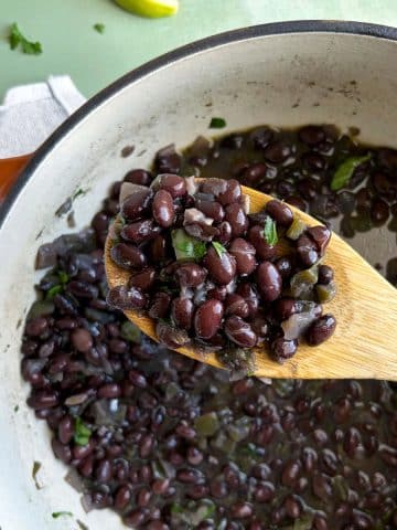 A wooden spoon holding up a scoop of Cuban-style black beans over the rest of the pot.