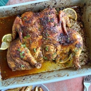 A baking dish with an entire roasted spatchcocked chicken and lemon slices inside.