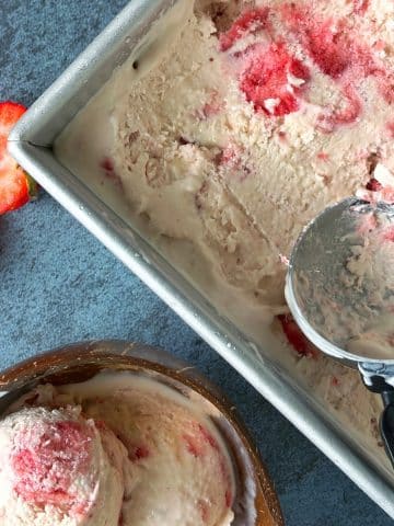 A loaf pan with homemade strawberry ice cream and a bowl with 3 scoops on the side.