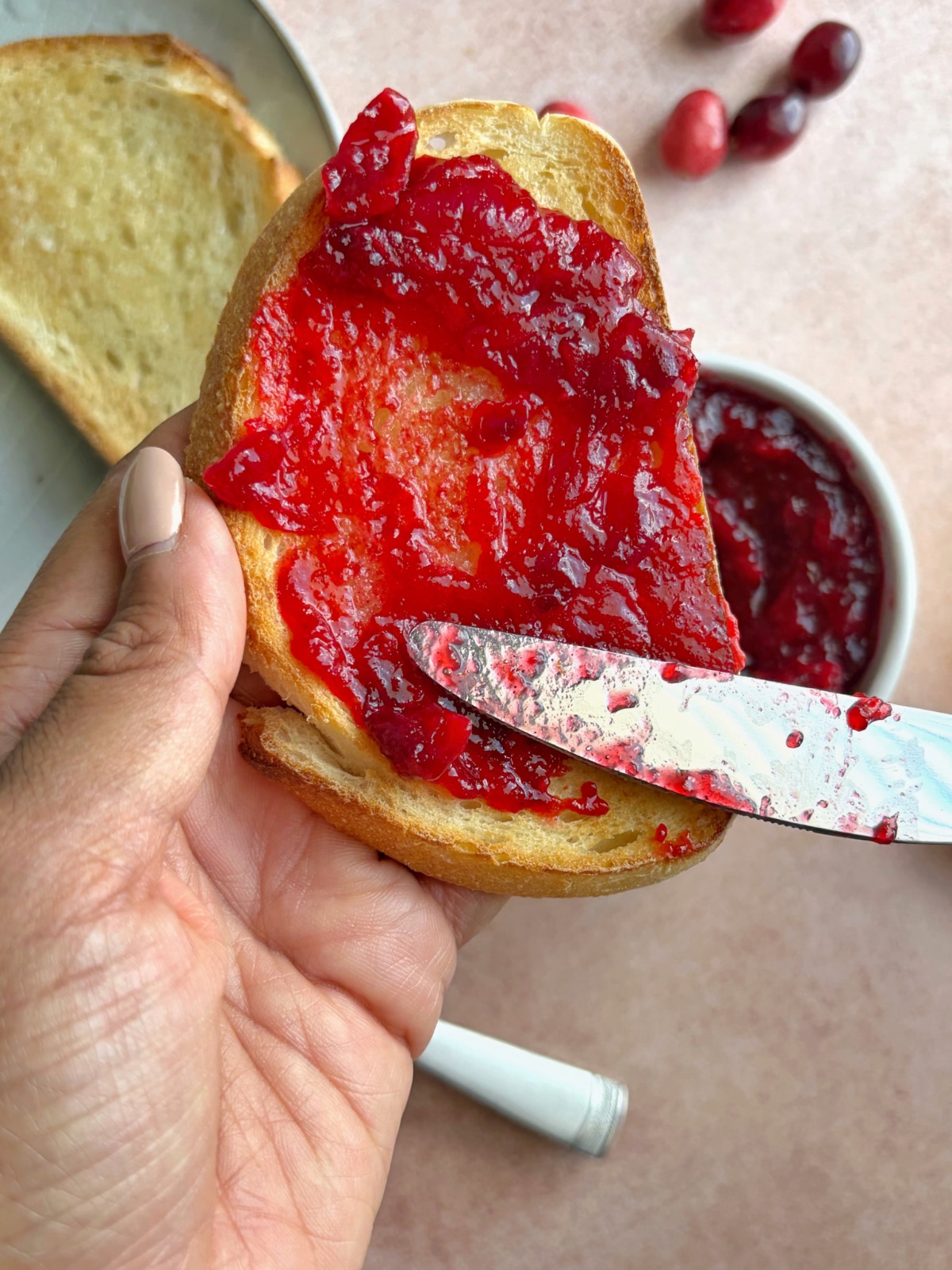 A hand spreading homemade cranberry orange jam onto a piece of sourdough toast.