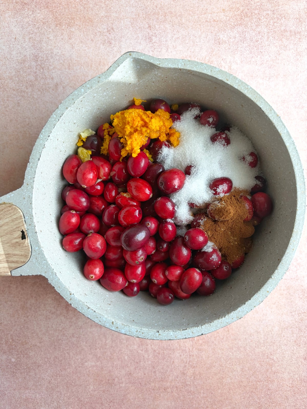A pot filled with cranberries, orange zest, sugar, and spices like cinnamon.