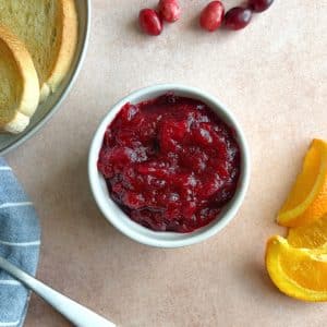 A bowl of cranberry orange jam with containers of toast and other ingredients on the side.
