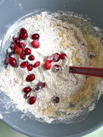 A mixing bowl with flour, cranberries, and wet ingredients before mixing.
