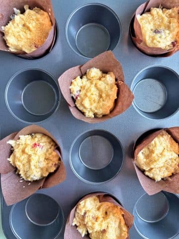 Muffin liners in a muffin pan filled with batter, before baking.