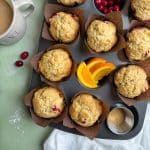 A muffin pan filled with baked cranberry orange muffins, and some ingredients in a few of the cups.