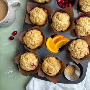 A muffin pan filled with baked cranberry orange muffins, and some ingredients in a few of the cups.