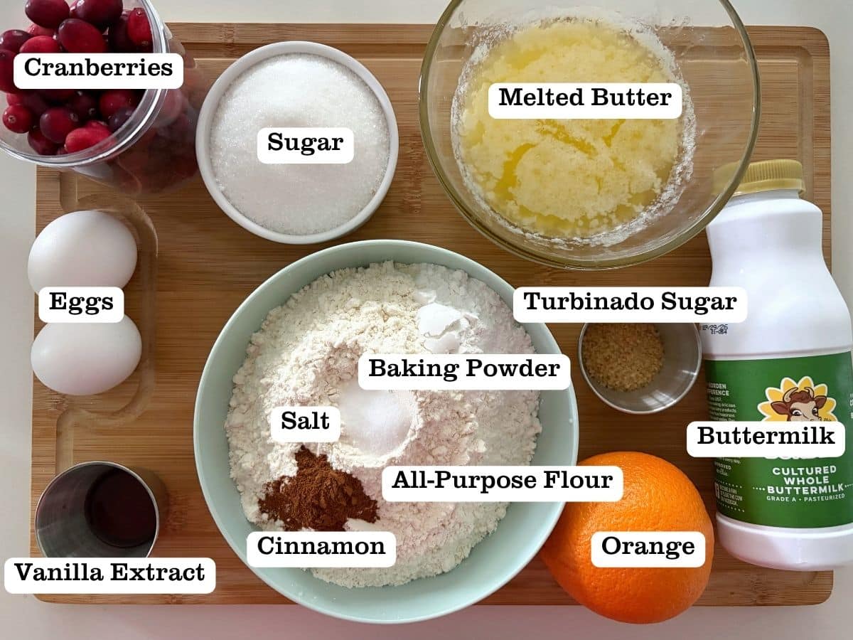 A board with containers of ingredients to bake cranberry orange muffins.