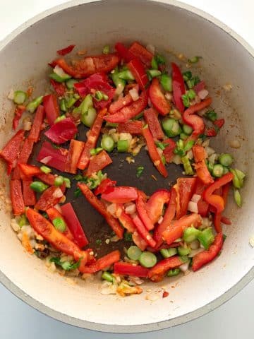 A skillet filled with chopped bell peppers, Thai chiles, and Chinese broccoli being sautéed.