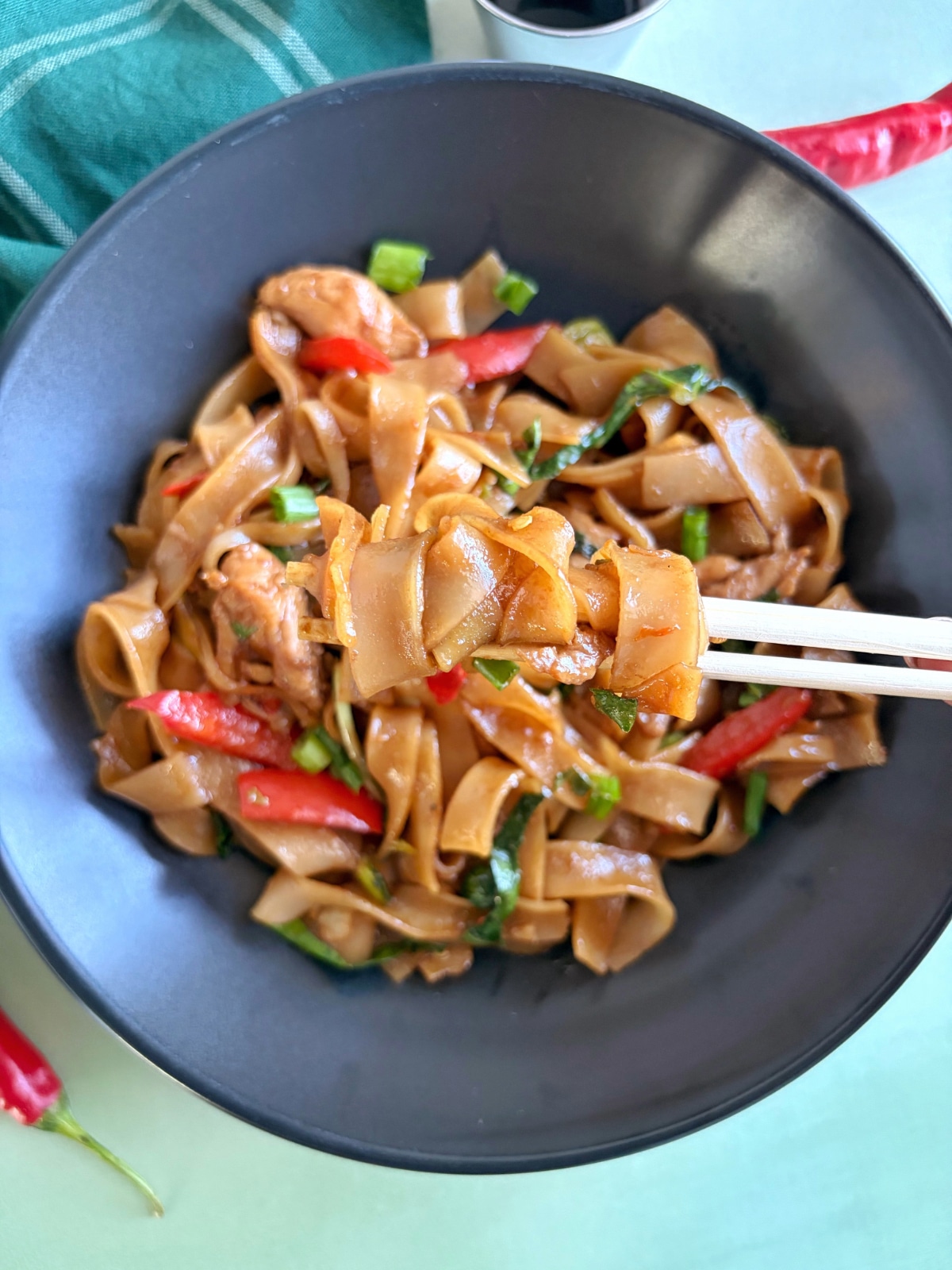 A pair of chopsticks lifting up a bite of drunken noodles over the rest of the bowl.
