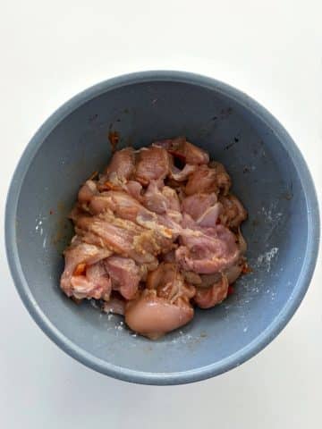 A mixing bowl of chopped chicken marinating in soy sauce.