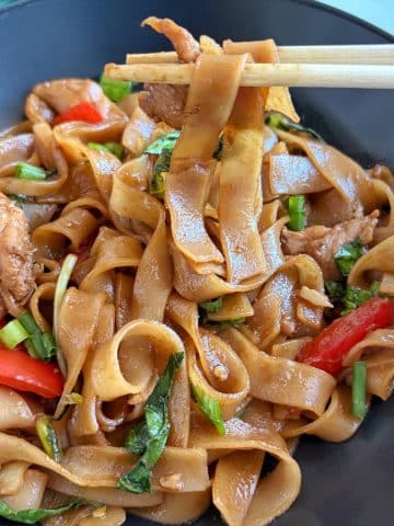 A bowl of pad kee Mao, or drunken noodles, with a pair of chopsticks picking up a bite.
