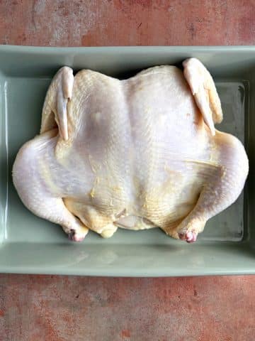 A spatchcocked chicken in a ceramic baking dish.